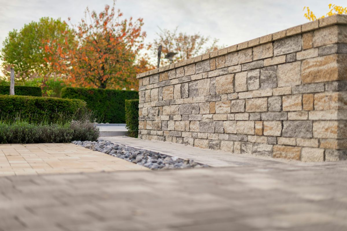 Natural stone garden wall beside a paver patio and clipped hedges